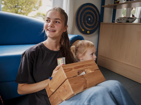 Eine junge Erzieherin in Ausbildung im Morgenkreis mit einer Materialkiste auf dem Schoß.
